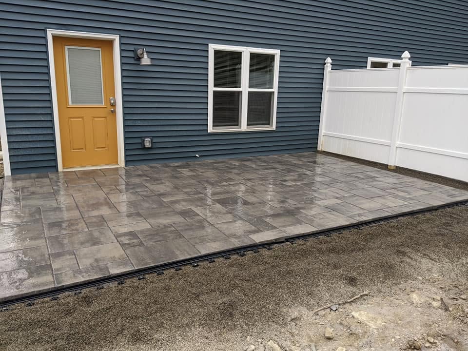Paver patio surface beside blue siding and a white privacy fence