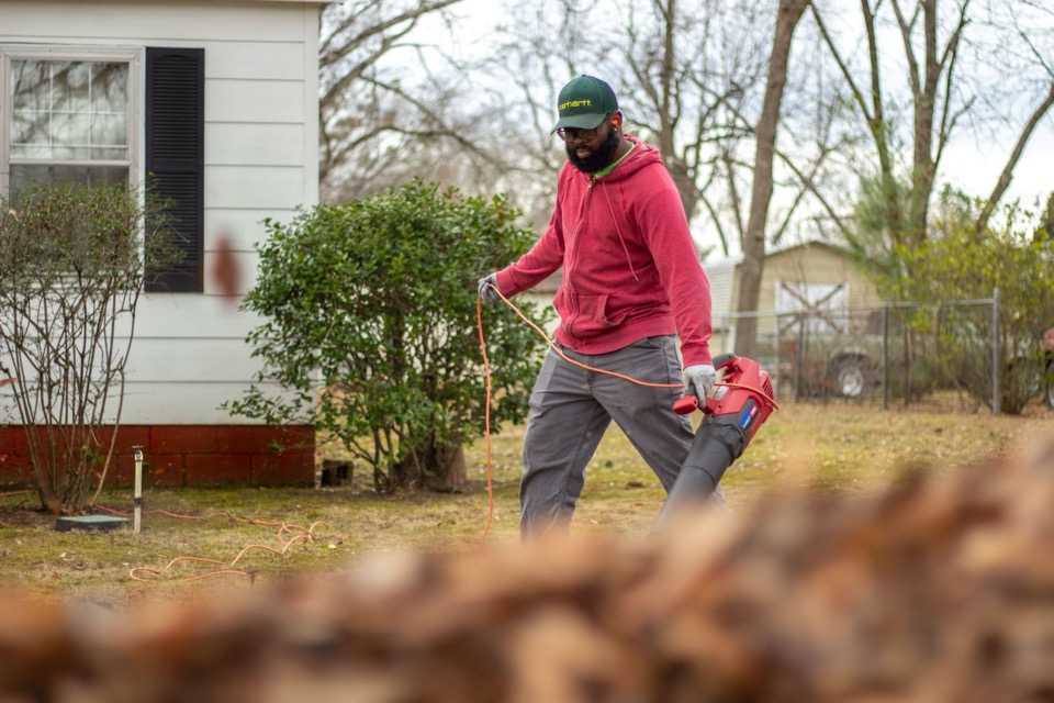 Person using a leaf blower to clear fallen leaves in a yard