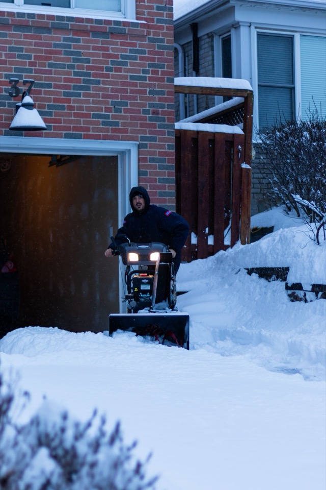 Person using a snow blower to clear a snowy residential driveway